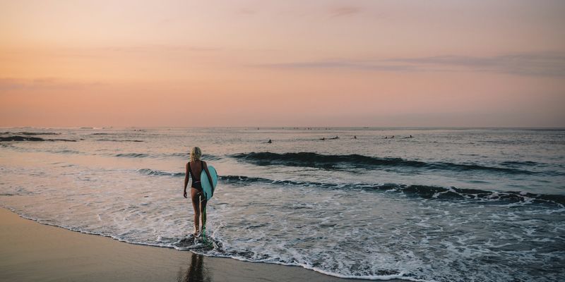 Chica con una tabla de surf caminando por la orilla al amanecer