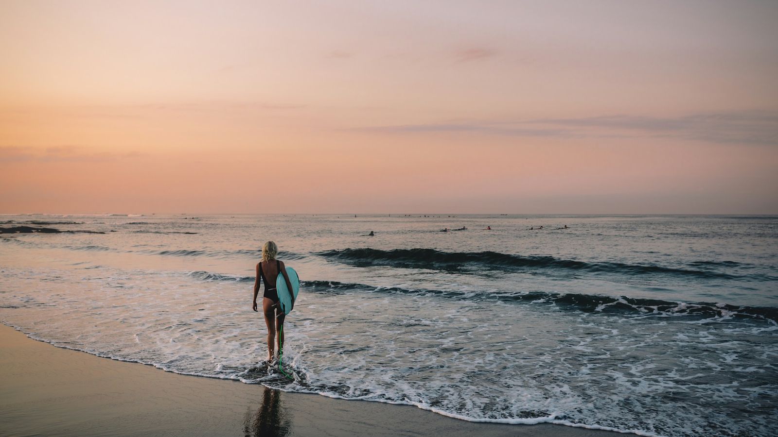 Chica con una tabla de surf caminando por la orilla al amanecer